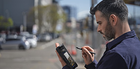 A man stands outdoors tapping on a Microsoft Surface with a stylus.