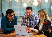 Three workers collaborate around a laptop in a modern office