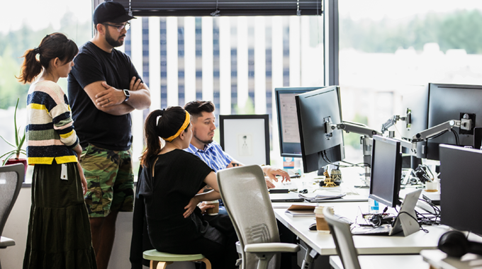 Four people, two women and two men, huddled around a computer collaborating.