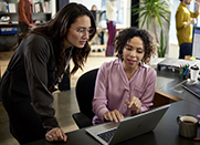 Two woman look at a computer monitor while collaborating.