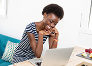 A woman smiles big while looking down at her laptop