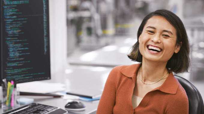 Smiling developer portrait in the context of automated assembly line location, working on screen to build intelligent apps powered by Azure